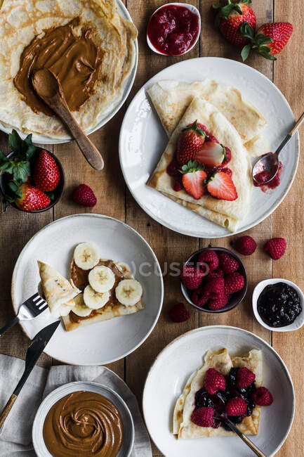 Von oben Teller mit leckeren Crêpes mit verschiedenen Belägen, die während des Frühstücks auf dem Holztisch liegen — Stockfoto