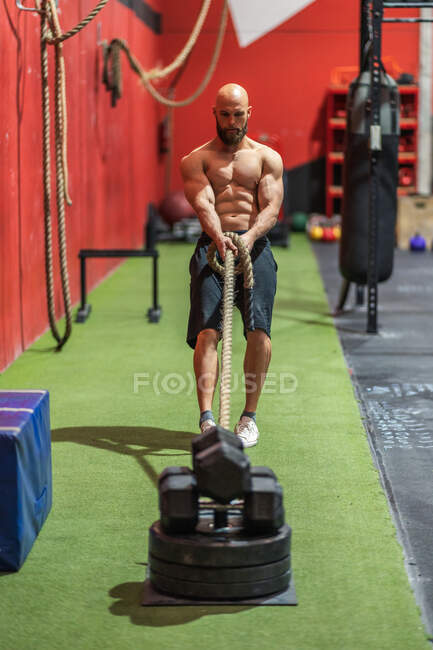 Сильный спортсмен тянет канат с тяжелыми грузами во время интенсивной тренировки в современном тренажерном зале — стоковое фото