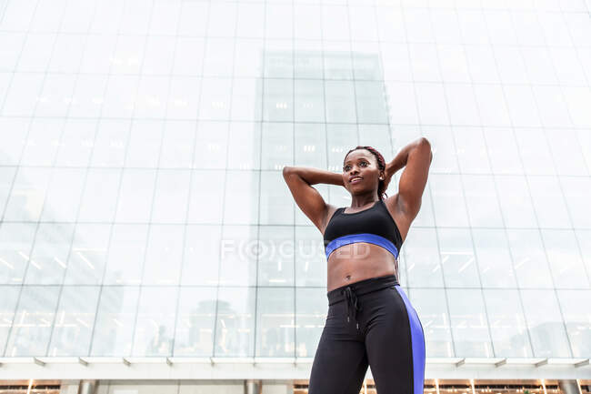 Young muscular African American woman in sportswear setting hair before workout on street — Stock Photo