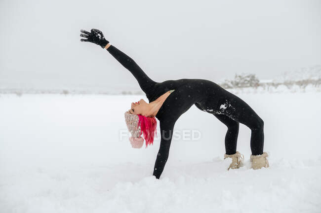Seitenansicht der anmutigen Frau praktiziert Yoga in Kapotasana auf schneebedecktem Feld im Winter — Stockfoto