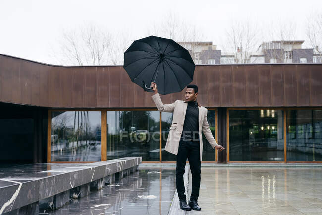 Porträt eines eleganten schwarzen Mannes mit grauem Mantel und Regenschirm auf der Straße — Stockfoto