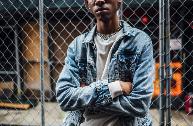 Crop preto na moda macho sério com corrente de prata no pescoço em casaco de ganga azul olhando para longe na rua — Fotografia de Stock