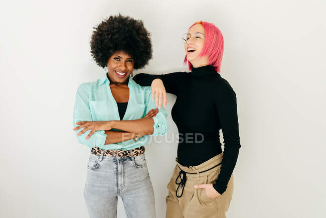 Joyeux jeune femme aux cheveux roses et petite amie afro-américaine en tenue élégante tout en s'amusant ensemble sur fond blanc — Photo de stock