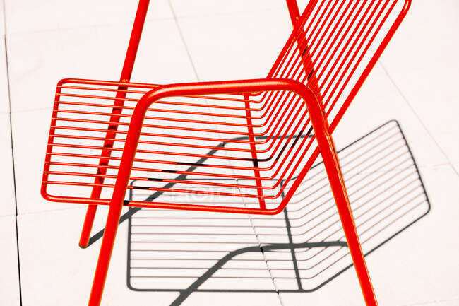 Летний красный металлический стул на белом полу при солнечном свете и тени — стоковое фото