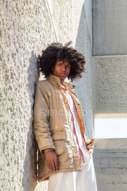From below side view African American male in vintage coat with Afro hairstyle standing on stairs while looking at camera — Stock Photo