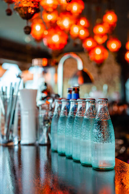 Glasflaschen mit kaltem Erfrischungswasser reihenweise auf Holztheke in Bar platziert — Stockfoto
