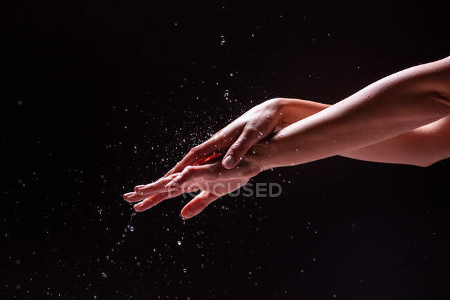 Schnittansicht einer anonymen Frau, die sich vor schwarzem Hintergrund Hände und Unterarm mit Spritzwasser wäscht — Stockfoto