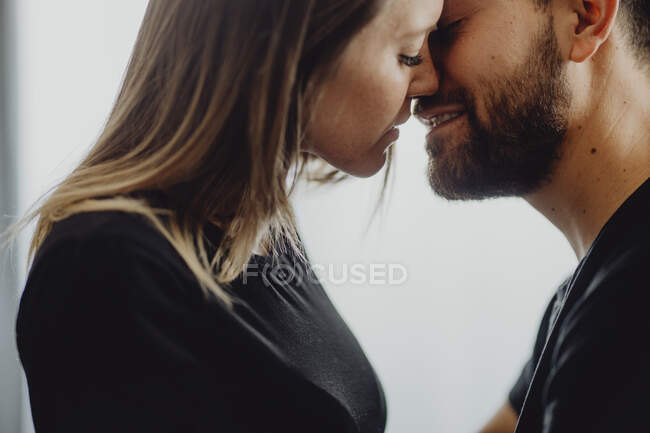 Mujer sonriente abrazando y besando a un hombre alegre en la frente mientras están sentados en un cómodo sofá en casa juntos - foto de stock