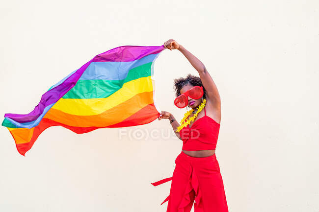 Stilvolle Afroamerikanerin in trendiger Kleidung und Brille mit bunter Fahne blickt während der Feier in die Kamera — Stockfoto