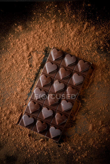 З верху цілого шоколадного батончика з окрасою серця, подається на чорному тлі з розсіяним порошком какао. — стокове фото
