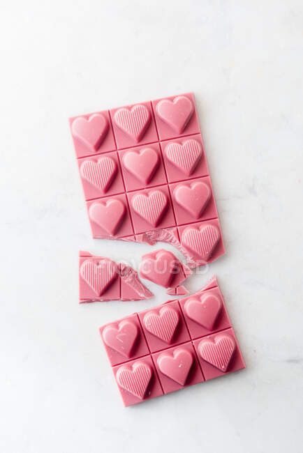 Top view minimalistic composition with pieces of handmade pink chocolate bar with heart shaped design on white background — Stock Photo