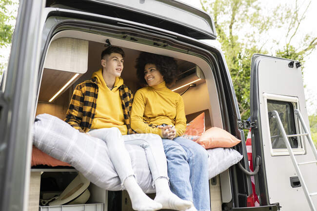 Щаслива чорна жінка посміхається і тримає руки з хлопцем, сидячи на ліжку всередині фургона у вихідний день у природі — стокове фото