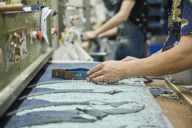 Detalle del trabajador que usa el patrón de corte mientras corta la tela en la fábrica de zapatos chinos - foto de stock