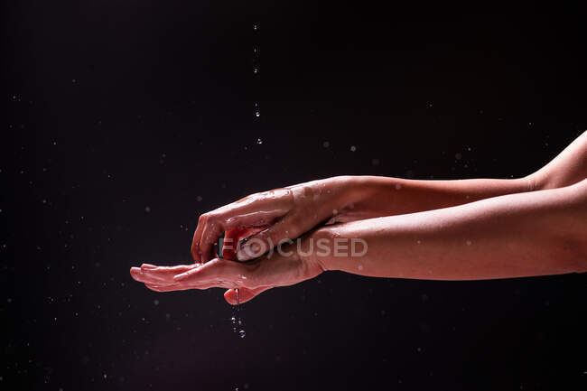 Vista de la cosecha de la mujer anónima lavándose las manos con agua salpicada contra fondo negro - foto de stock