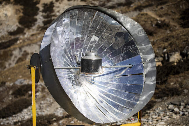 Eau bouillante dans une bouilloire métallique placée sur une cuisinière solaire sur un sol rocheux dans les montagnes de l'Himalaya au Népal par une journée ensoleillée — Photo de stock
