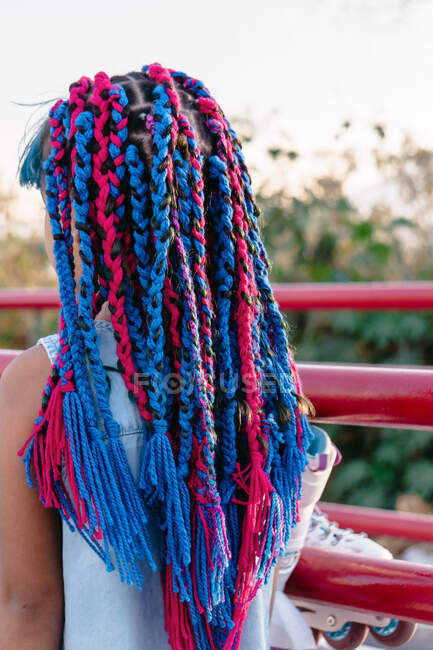 Back view of anonymous Mexican kid with colorful braids admiring trees while standing near fence in evening — Stock Photo