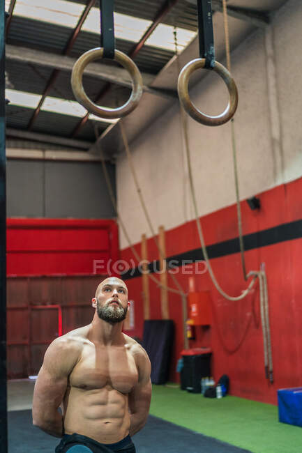 Uomo muscoloso barbuto guardando in alto mentre in piedi vicino alle attrezzature durante l'allenamento in palestra moderna — Foto stock