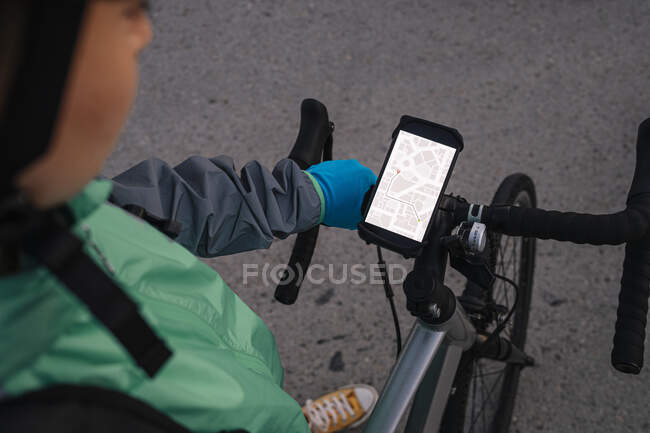Desde arriba mensajero anónimo examinar ruta en el mapa GPS antes de montar en bicicleta en la calle de la ciudad - foto de stock