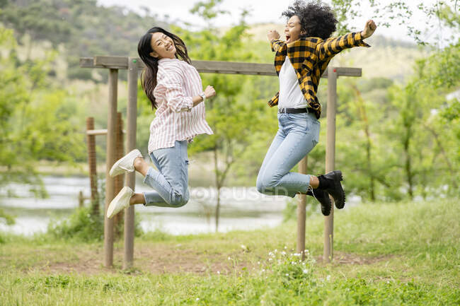Пара лесбиянок-мультиэтнических женщин, прыгающих над землей в лесу и наслаждающихся вместе свободой — стоковое фото