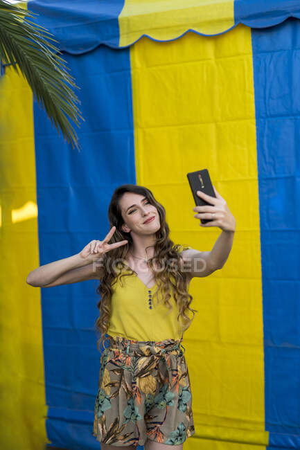 Glückliche Frau mit welligem Haar macht Selfie mit Handy, während sie auf zwei farbigen Hintergrund auf der Straße lacht — Stockfoto