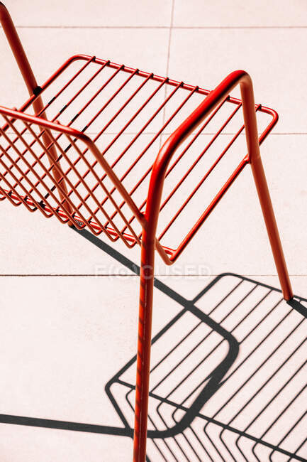 Літній відкритий червоний металевий стілець, розміщений на білій підлозі на сонячному світлі з тіні — стокове фото