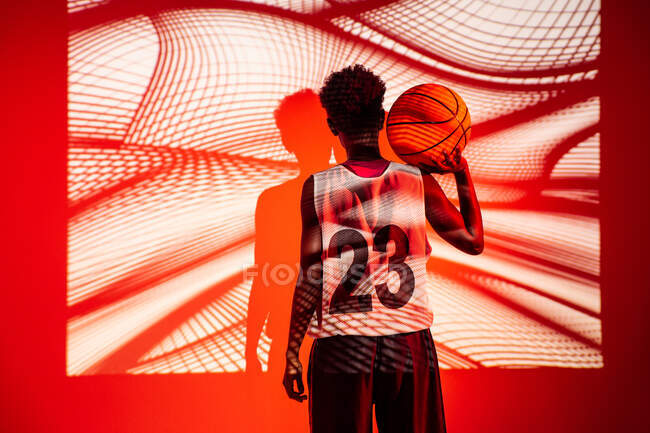 Чорна жінка з баскетбольним обладнанням у студії за допомогою кольорових гелів і проекторів вогні над помаранчевим фоном — стокове фото