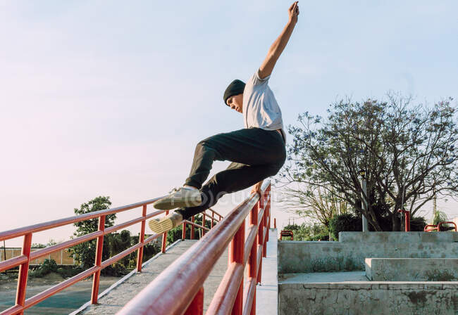 Jovem destemido de baixo ângulo pulando acima do corrimão de metal na cidade enquanto executa acrobacia de parkour no dia ensolarado — Fotografia de Stock