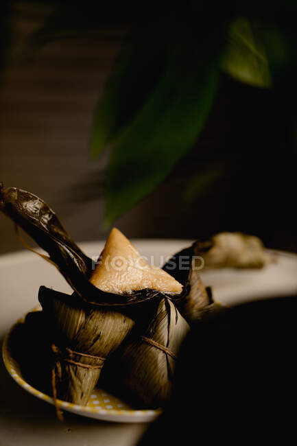 Boulettes de riz à feuilles de bambou ouvertes et couvertes placées sur une assiette à carreaux mignonne — Photo de stock