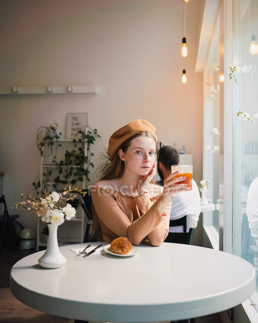 Mulher francesa na boina sentada à mesa no café com um copo aromático de café e croissant recém-assado — Fotografia de Stock