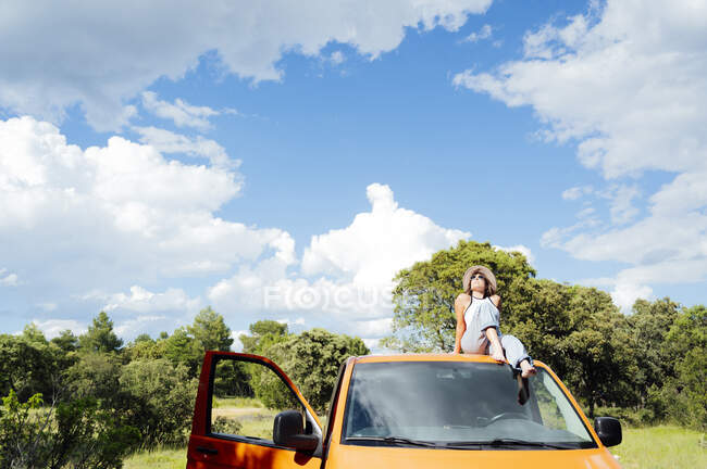 Середина жінка-дослідник сидить на даху фургона і насолоджується літніми пригодами в сонячний день — стокове фото
