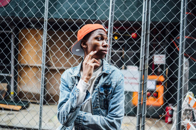 Crop black homme sérieux tendance avec chaîne argentée sur le cou en denim bleu veste regardant loin dans la rue — Photo de stock