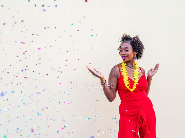 Femme afro-américaine excitée avec les bras tendus et la bouche ouverte debout sous des confettis tombants à l'événement sur fond blanc — Photo de stock