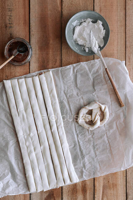 De arriba pretzel crudo y rollos de masa colocados sobre papel cerca de mermelada de higo y queso crema sobre madera aserrada - foto de stock