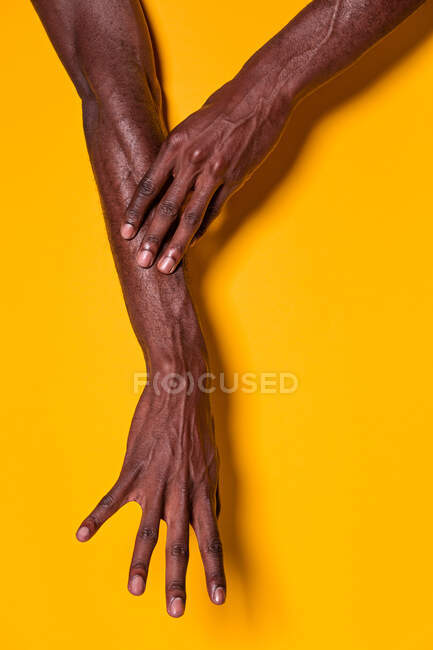 Corte vista de anônimo muscular preto homem tocando seu antebraço com a mão no fundo amarelo — Fotografia de Stock