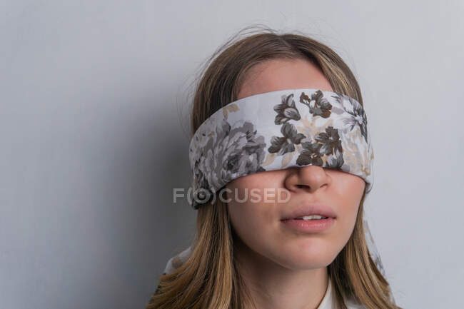 Giovane donna dai capelli biondi in camicetta elegante che copre gli occhi con sciarpa di seta piegata con ornamento floreale su sfondo bianco — Foto stock