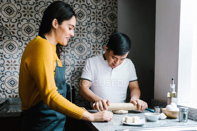Любляча етнічна мати і хлопчик-підліток з синдромом Дауна готують тісто, готуючи разом на кухні вдома — стокове фото