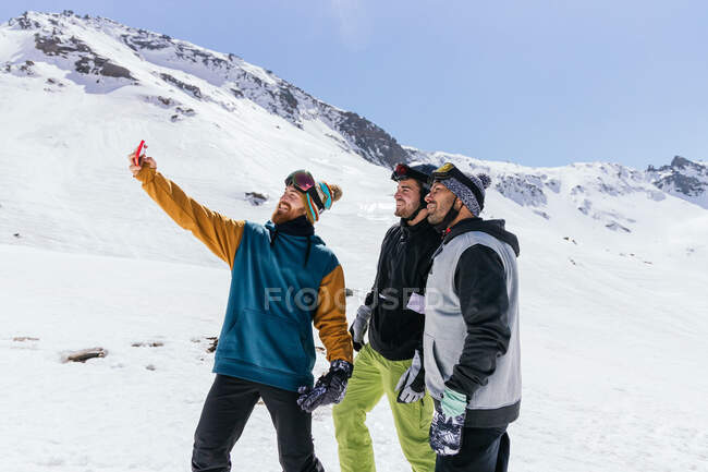 Conteúdo amigos do sexo masculino em roupas esportivas tomando auto-retrato no celular contra a Sierra Nevada no inverno — Fotografia de Stock