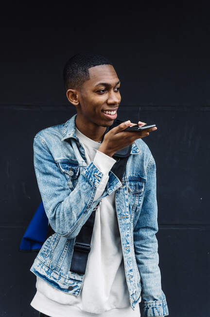 Side view of a young black man with mobile and backpack on the street while leaving a voicemail — Stock Photo
