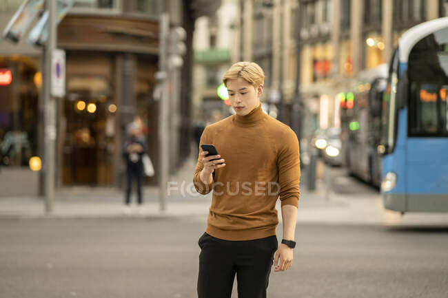 Focado étnico elegante masculino em pé na rua e mensagens no telefone celular nas mídias sociais — Fotografia de Stock