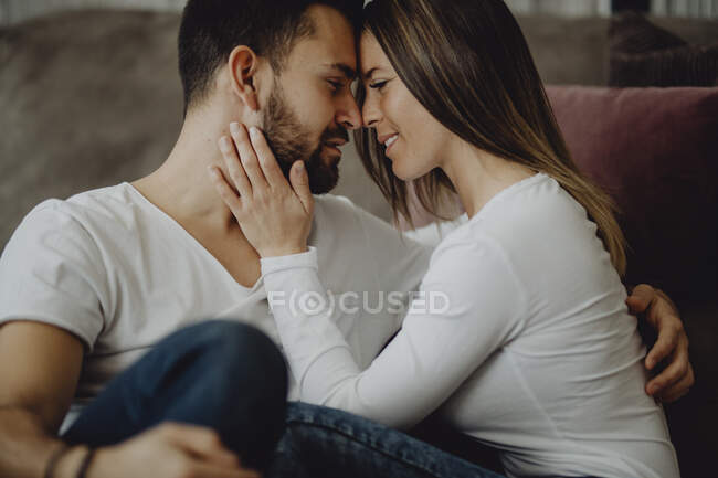 Smiling female embracing and kissing cheerful man in forehead while sitting on floor — Stock Photo