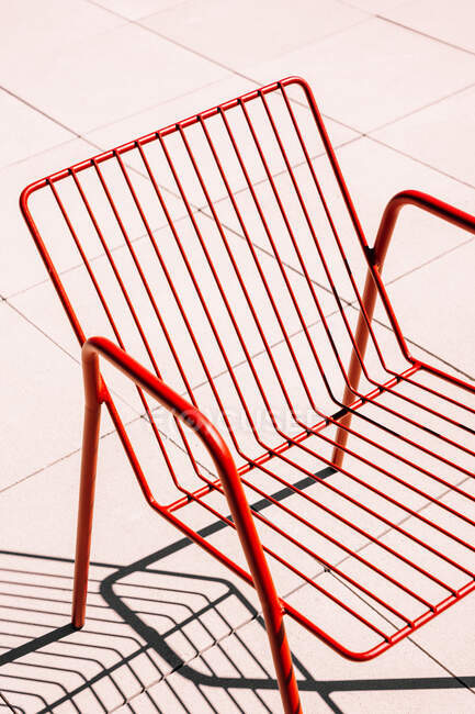 Chaise extérieure en métal rouge d'été placée sur un sol blanc à la lumière du soleil avec ombre — Photo de stock