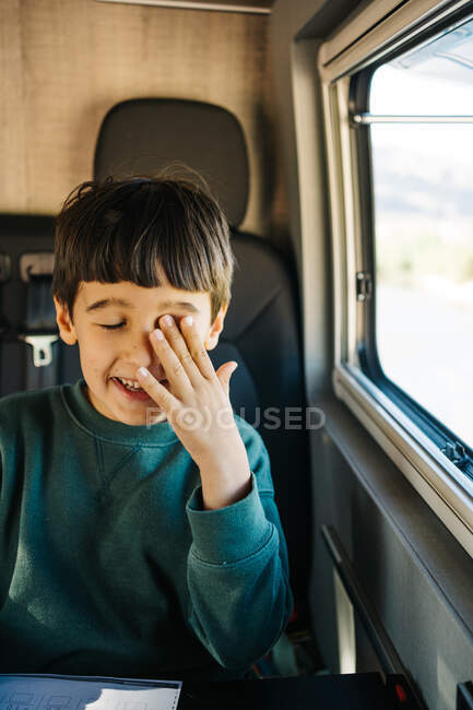 Menino sentado dentro de uma caravana enquanto coça o olho — Fotografia de Stock