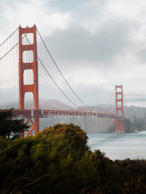 Célèbre Golden Gate pont suspendu au-dessus de la rivière avec rivage vert sous un ciel gris sombre à San Francisco — Photo de stock