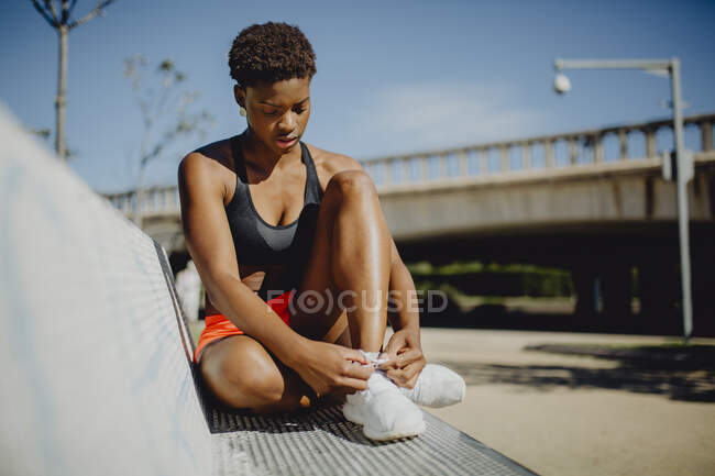 Jeune femme afro-américaine de remise en forme au repos et attacher les lacets après avoir fait de l'exercice sur le banc du parc — Photo de stock