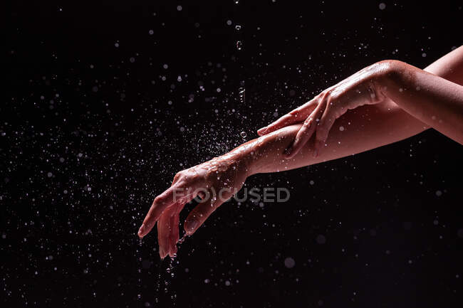Vista ritaglio di donna anonima lavarsi le mani e l'avambraccio con spruzzi d'acqua su sfondo nero — Foto stock