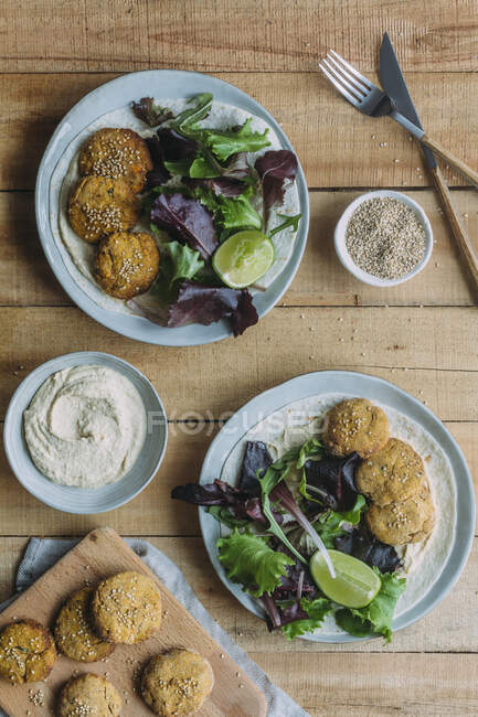 Plates with fresh lettuce salad and sweet potato falafel near sauce and sesame on wooden table — Stock Photo