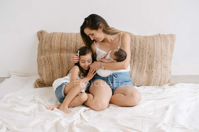 Carino bambina seduta con la madre gentile che tiene il bambino appena nato mentre si siede sul divano a casa — Foto stock