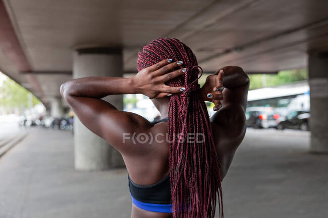 Back view of ethnic sportswoman setting hair and preparing to workout on parking lot — Stock Photo