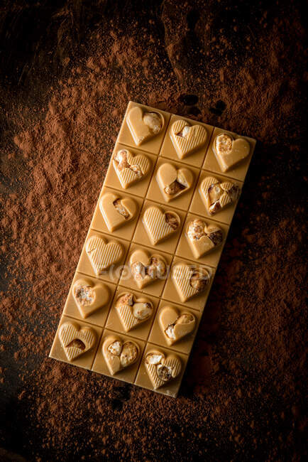 Desde arriba de la barra de chocolate entero con decoración en forma de corazón servido sobre fondo negro con cacao en polvo disperso - foto de stock