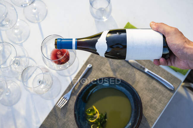 Camarero vertiendo vino tinto en una copa en el restaurante de alta cocina al aire libre - foto de stock